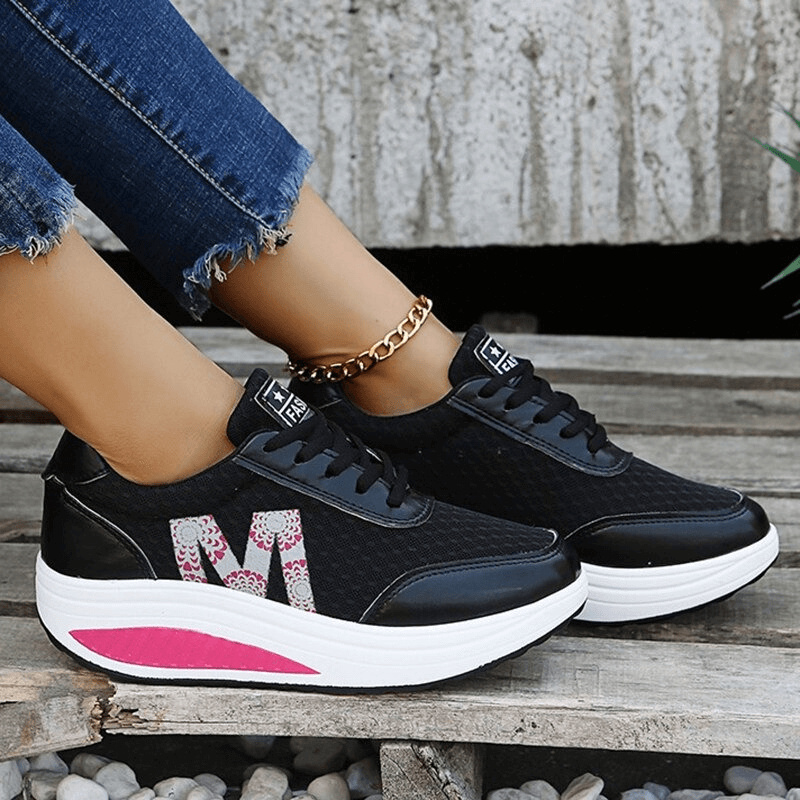 Black breathable mesh sneakers with thick white sole and pink detail, worn with jeans. Casual, stylish lace-up shoes.